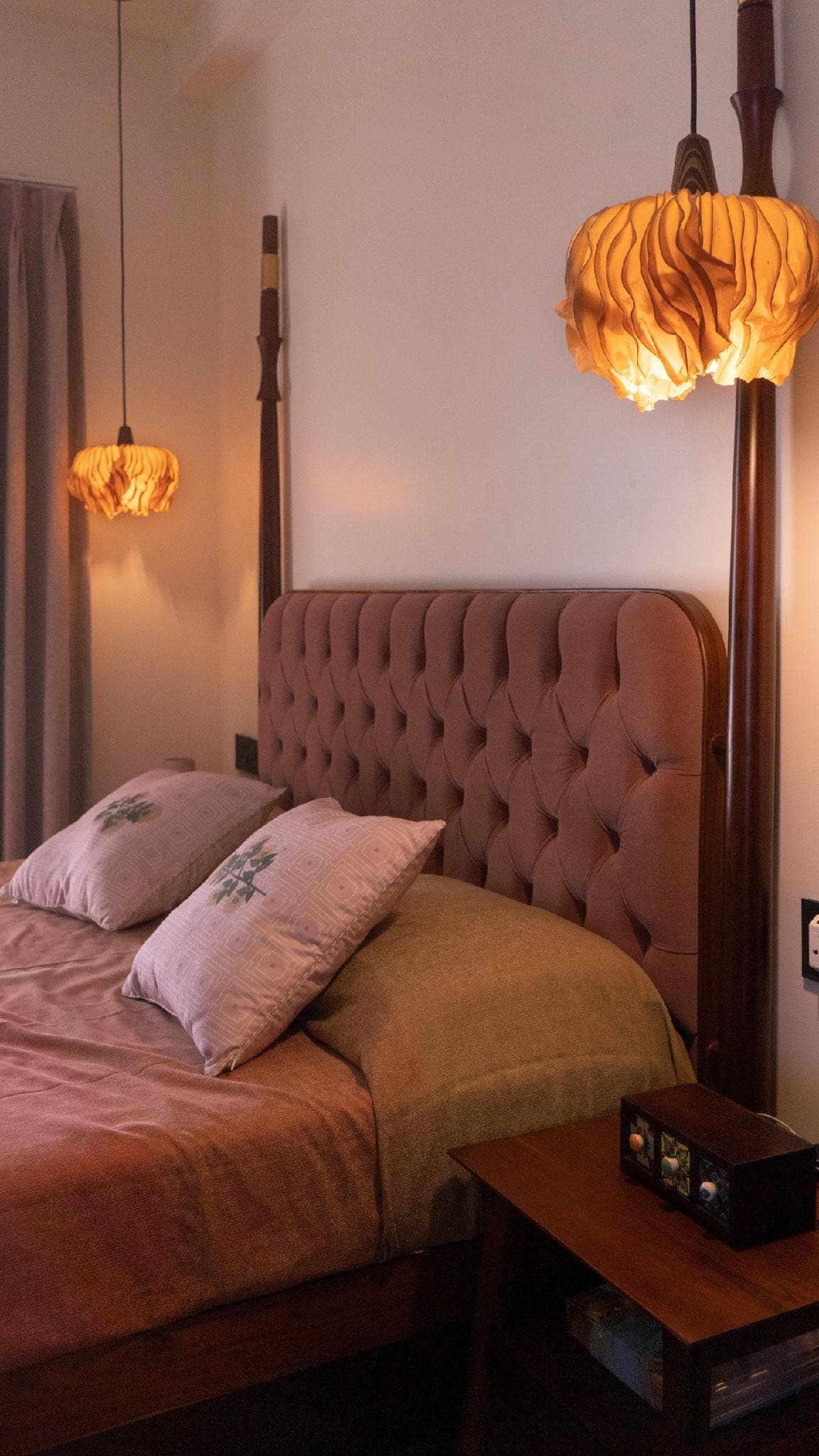 A four-poster bed lit by two sculptural fabric pendant lights.