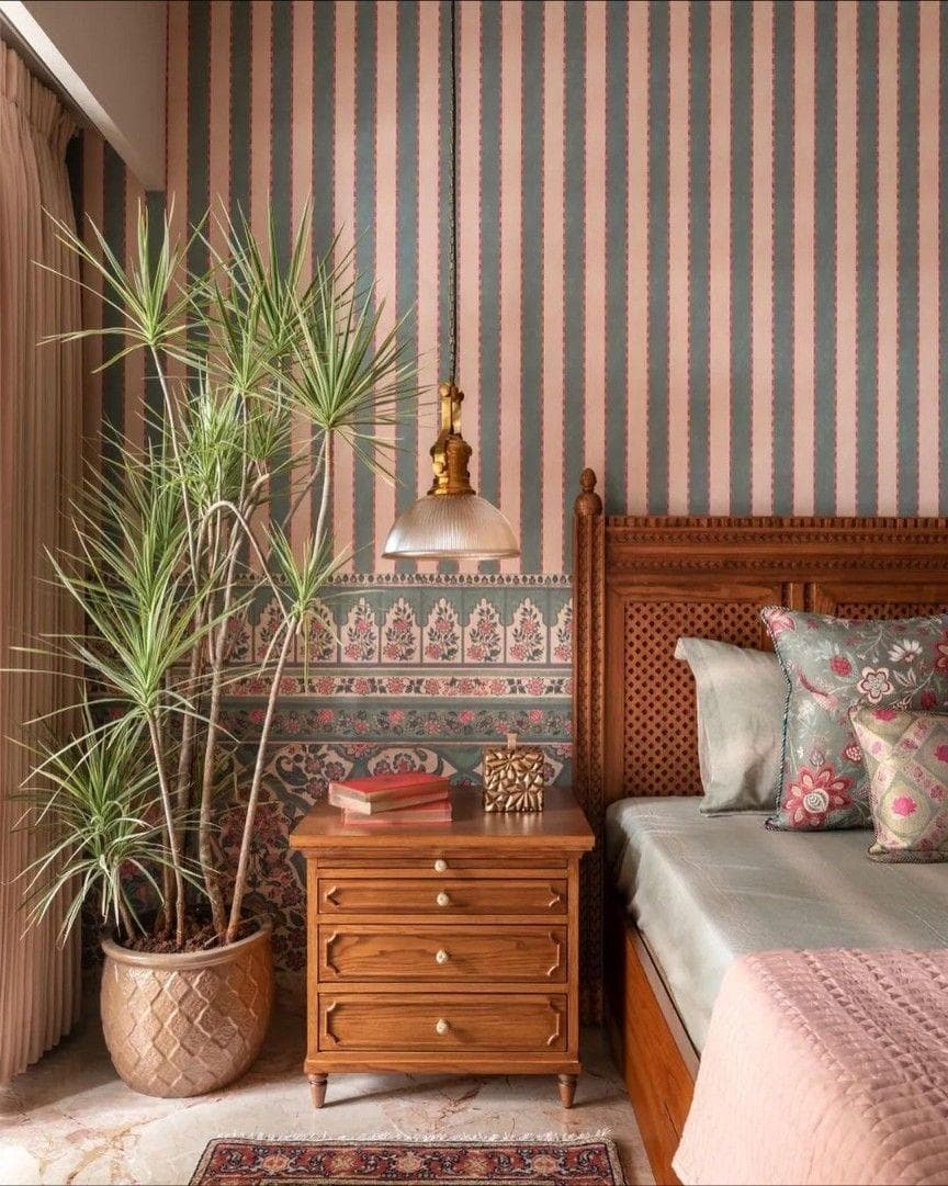 A bedroom with striped wallpaper, a carved wood headboard, and a brass pendant light beside a potted plant.