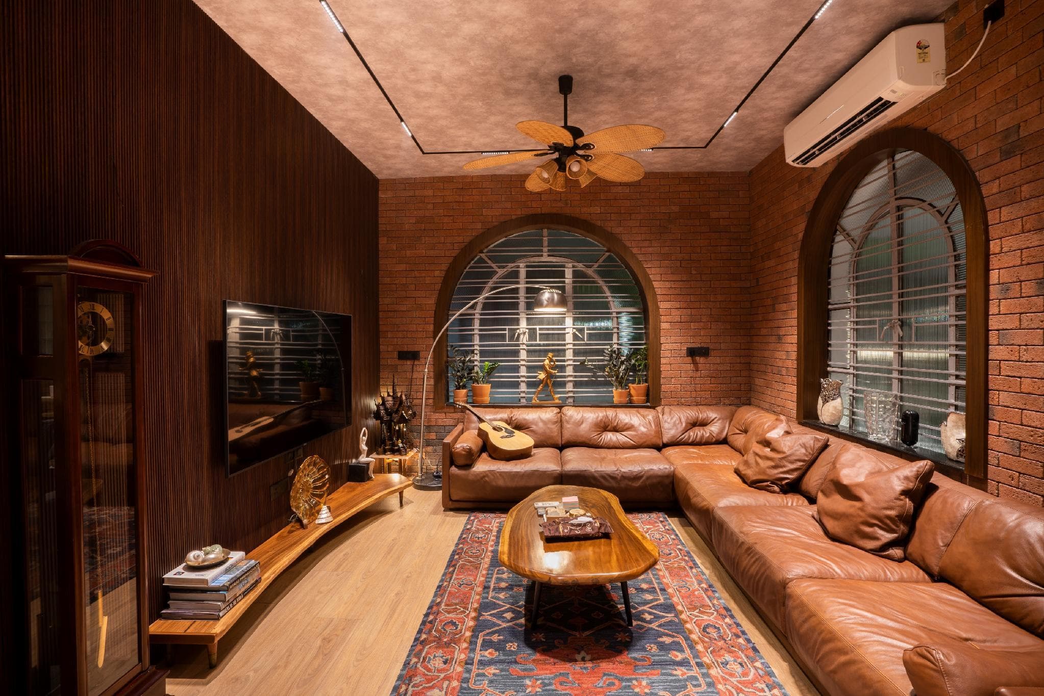 A living room with exposed brick walls, arched windows, and a tan leather sectional sofa.