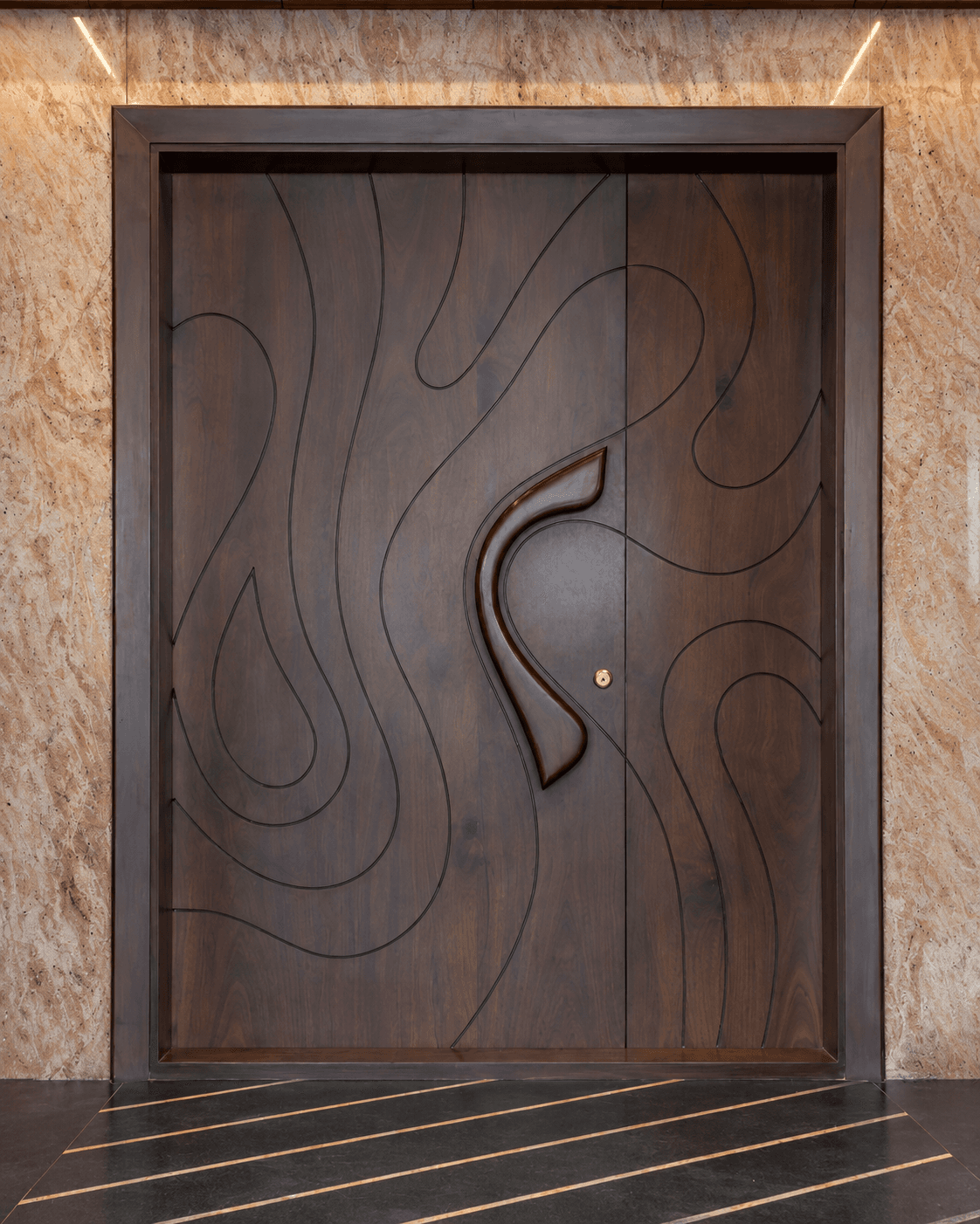 Sculptural Curve Double Main Door in a luxury marble-clad entrance, featuring dark wood, sweeping engraved curves and a sculptural central pull.