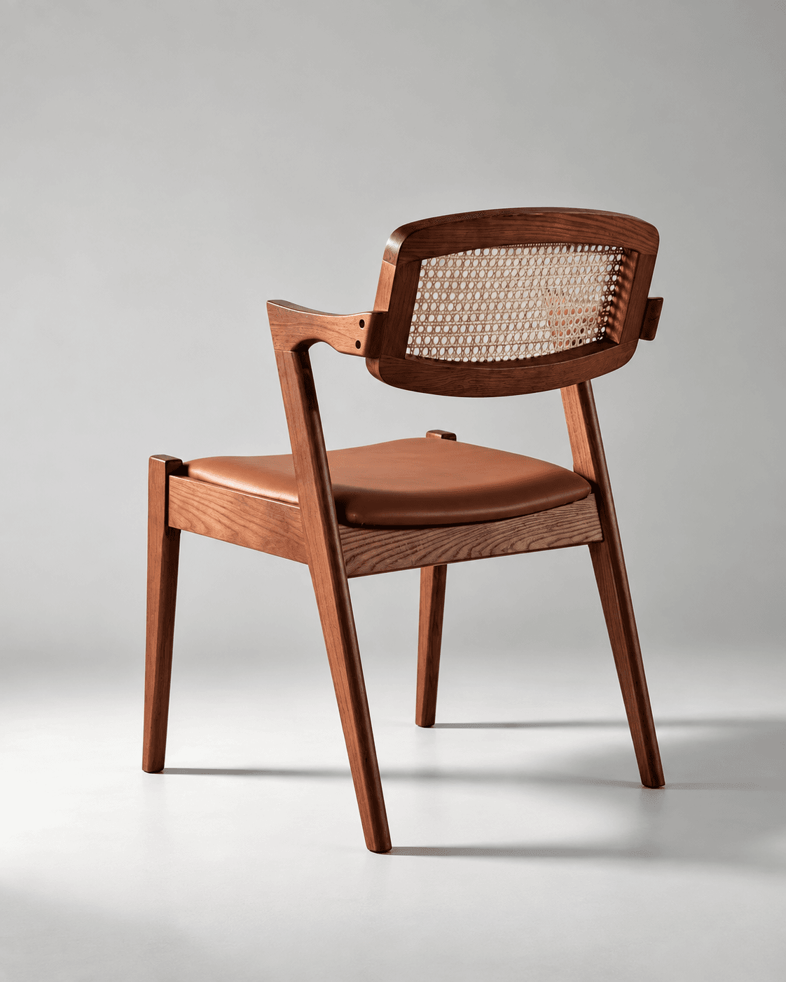 NOÉ premium cane dining armchair with sculpted wooden frame, natural cane backrest and brown leatherette seat in a neutral interior.
