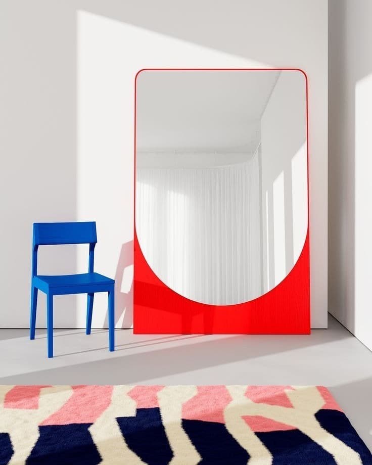 VÉRTICE red sculptural floor mirror styled in a contemporary interior with a blue chair.