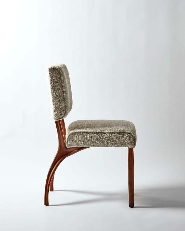 AUREL premium dining chair with a sculptural walnut wooden frame and softly upholstered beige seat and backrest on a light studio background.
